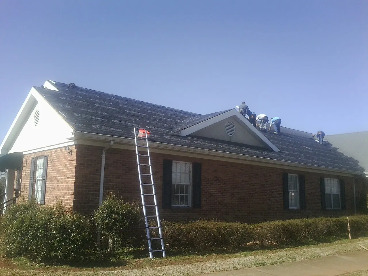 Crew tearing shingles off a brick ranch roof with a ladder set — Emergency Roof Repair work by our crew in Dorchester
