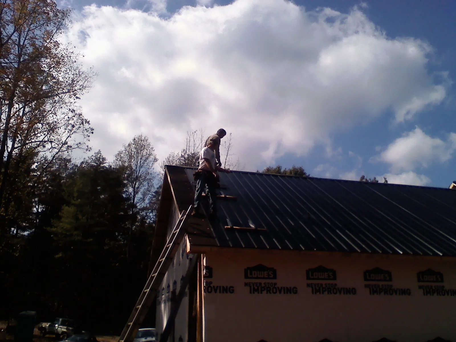 Roofer fastening dark metal panels high against a cloudy sky, from a Roof Inspection job in Dorchester